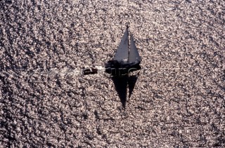 A solitude cruising yacht in silhouette sails across a metallic texture open sea