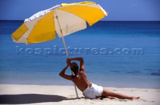 Model under shade of umbrella on sandy beach