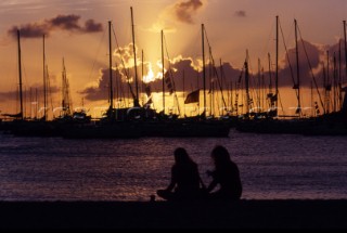Couple watching sunrise through masts in a marina.