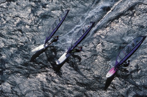 Three windsurfers race across the water