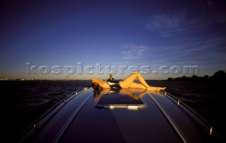 Sexy girl female model in black leather swimsuit onboard a fast sleek powerboat driven by a romantic man