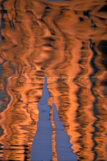 Fire water. Orange and black artistic reflections of white sails on the surface of the sea.
