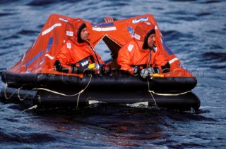 Two crew in red survival suits in a life raft awaiting rescue