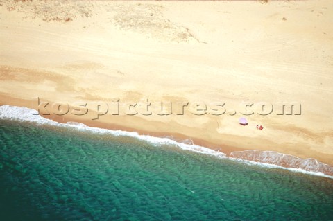 Aerial view of a couple sitting on a deserted beach by the shade of an umbrella