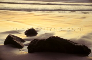 Rocks on sandy beach at sunset