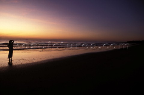 Woman on beach gazing out to sea at sunset