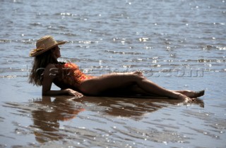 Woman in straw hat lying in wet sand on beach