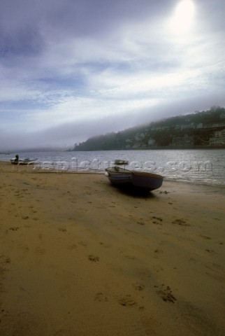 Dinghy on sand at Salcombe Estuary with mist on hills in distance UK