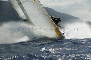 Crew on windward rail of yacht crashing through wave in choppy seas.