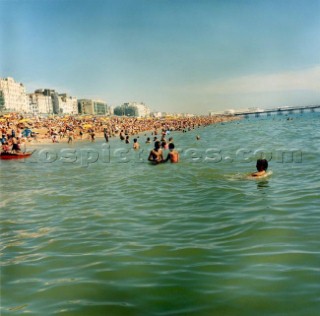 People playing in sea off crowded pebble beach, Brighton