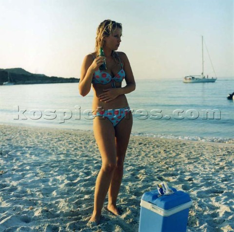 Girl in bikini standing on sandy beach with bottle of beer Corscia