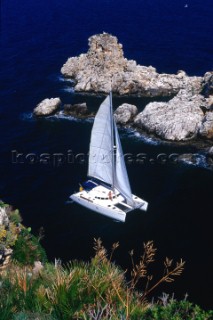 Sicily Italy. A lady lounges on the deck of a catamaran as it sails into a channel