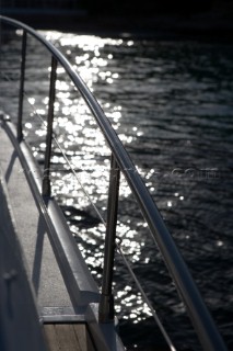 Sunlight reflects from the water beyond the rail of a yacht