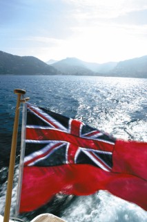 Red ensign flying from rear of power boat on lake with mountain backdrop
