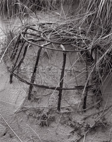 Old lobster pot semiimmersed in sand which has texture from rain drops Marram grass resting on top a