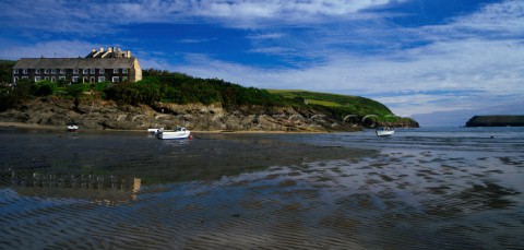 Traditional cottages on a headland are reflected in the wet sand at Hawkers Bay in the Camel Estuary