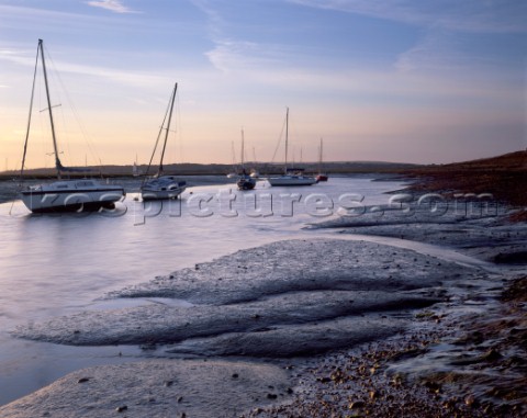 Tide ebbs near Keyhaven leaving shimmering mud and pebbles catching the first rays of sun Yachts dry