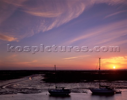 Sunrise with sweeping high level cloud Foreground yachts and meandering stream with wet reflective m