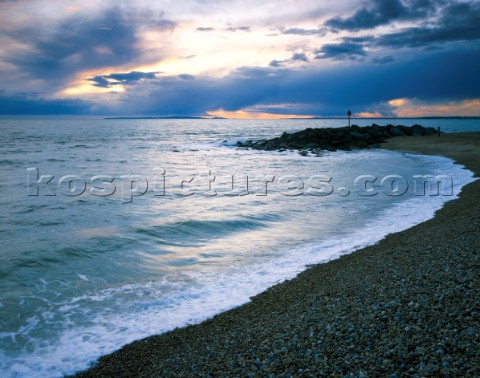 View along the beach at Hurst showing sea defences and darmatic sky over the Dorset coast in the dis