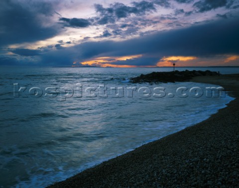 View along the beach at Hurst showing sea defences and darmatic sky over the Dorset coast in the dis