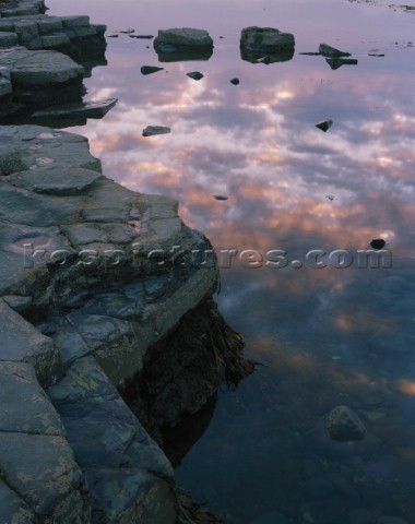 Soft evening light and reflections of a colourful sky in a calm sea alongside the Ledges and boulder