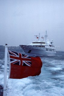 British ensign on stern of power boat with superyacht in background