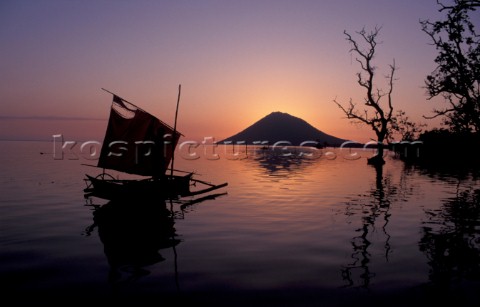 Small fishing sail boat at sunset withManado Tua volcano in backgroundBunaken IslandIndonesia