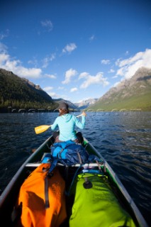 A woman in the bow of a fully loaded canoe, paddling across Bowman Lake in Glacier National Park, Montana.