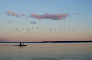 A sea kayaker paddles across Sebago lake at dusk on the outskirts of Portland Maine.