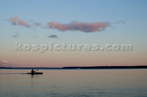 A sea kayaker paddles across Sebago lake at dusk on the outskirts of Portland Maine