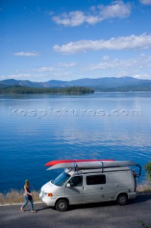 Holly Walker takes a break along the shoreline of Priest Lake on a road trip in northern Idaho. The image shows Walker walking back to her camper van loaded with sea kayaks and bikes. Priest Lake, Idaho.