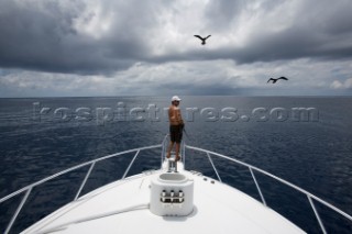 Wide view of a man fishing off the bow of a boat with a bird and dark clouds overhead in Costa Rica.
