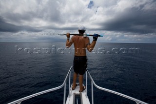 A man with a fishing pole resting on his shoulders, looking out at the ocean with dark clouds overhead in Costa Rica.