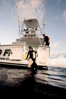 A woman wearing goggles, snorkel and flippers sits on the edge of a boats dive door, preparing for a dive in the waters of Costa Rica.