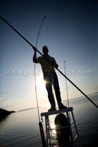 A flats boat captain poles through shallow water in the Everglades while silhouetted by the sun at d