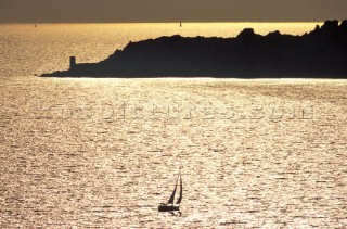 A silhouette cruising yacht sails towards a headland in the gold sunset