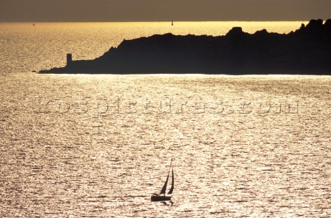 A silhouette cruising yacht sails towards a headland in the gold sunset 