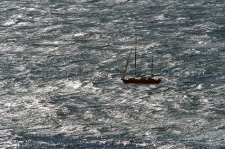 A lone motor sailer flying a jib crosses a rough metallic sea