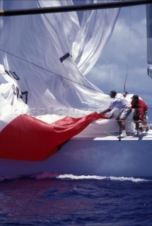 Two crew members gather a huge spinnaker sail onboard