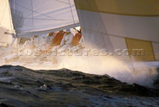 Crew on rail of racing yacht covered in spray from rough sea