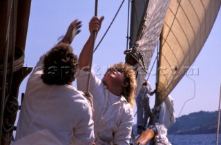 Two crew members hoist a sail onboard a classic yacht