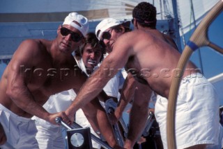Two bare chested men working a coffee grinder winch onboard a racing yacht
