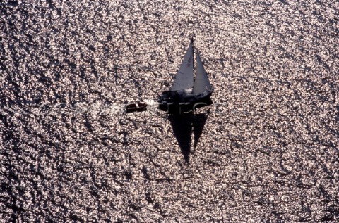 A solitude cruising yacht in silhouette sails across a metallic texture open sea 