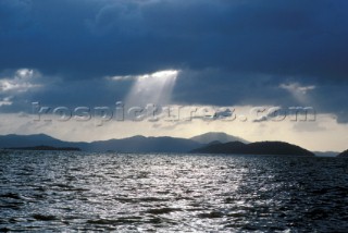 Suns rays through clouds over silhouetted islands
