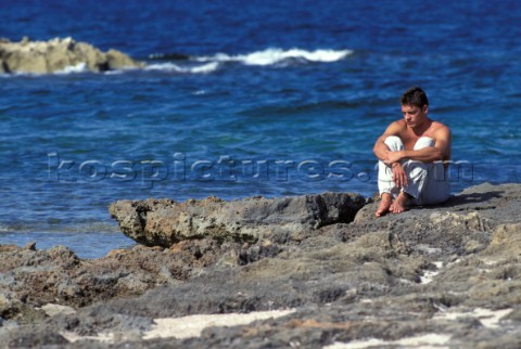 Fit man sitting on ragged rocks near the sea in pensive moment