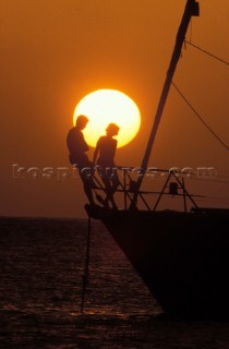 Couple on bow of anchored yacht at sunset.