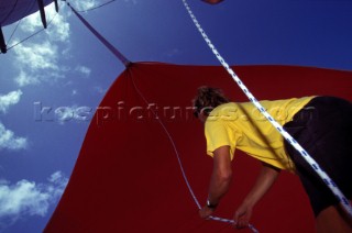 Crew member removes caught halyard from around red spinnaker