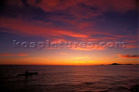 Canoeist paddling against a crimson sunrise sky Baja California