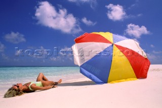Woman lying on beach by colourful umbrella