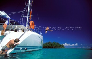 Boy jumping off the side of a catamaran into the sea
